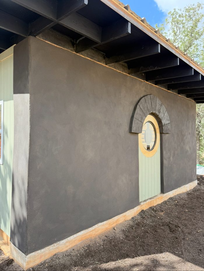 Charcoal clay plaster exterior with arched round window