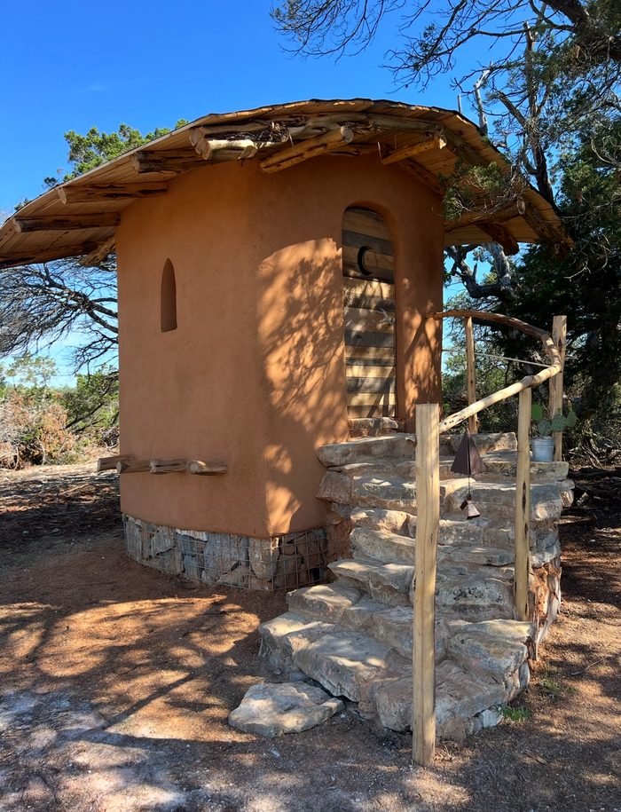 Round cob structure in clay plaster with stone steps and cedar roof