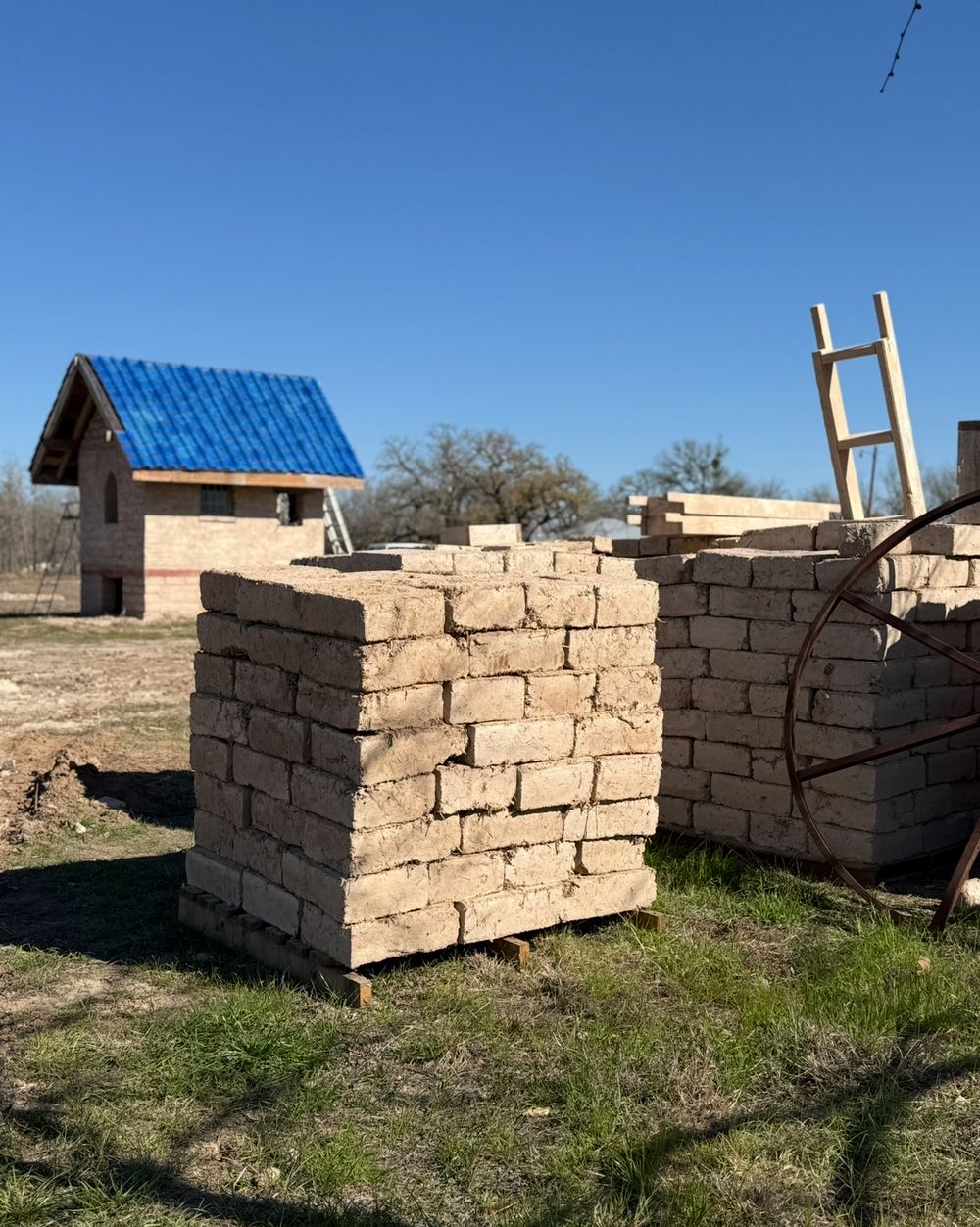 Stacked pallets of adobe bricks on site beside a finished building