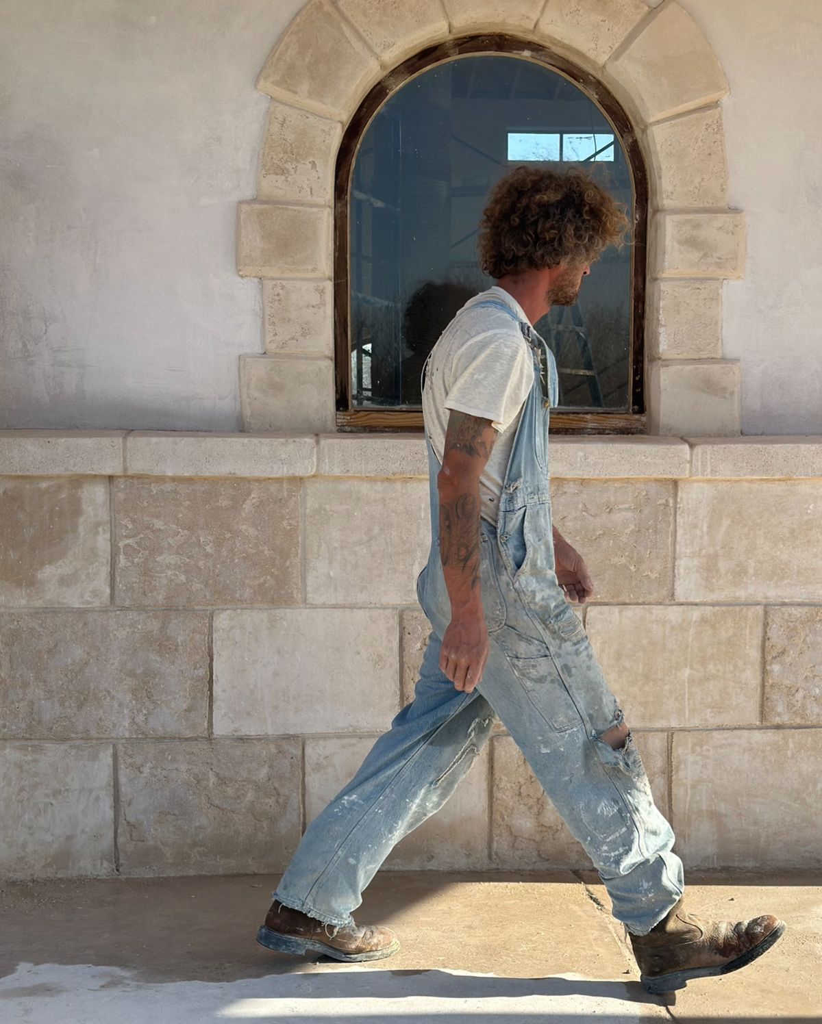 Plasterer in work overalls walking past a limestone wall and arched window