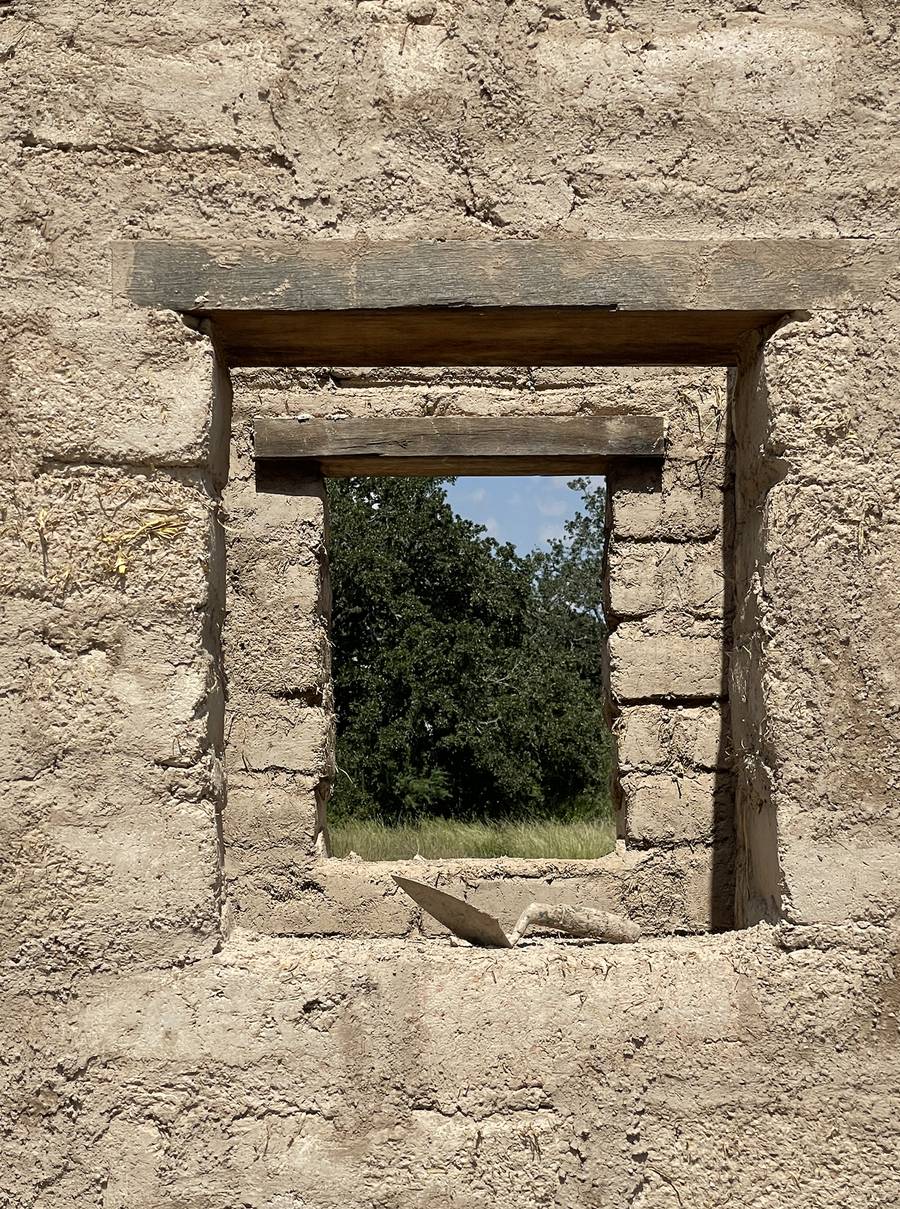 Adobe wall with a timber lintel window opening and a trowel resting on the sill